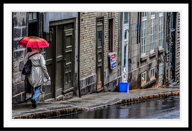 A person walking down the street with a red umbrella.